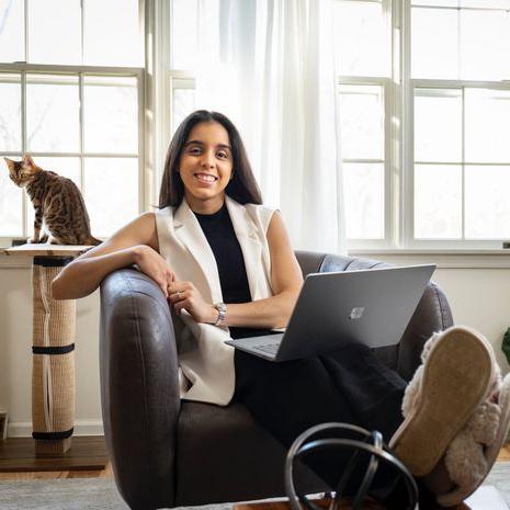 An image of Loymi Peralta Cruz smiling while sitting and holding her open laptop.